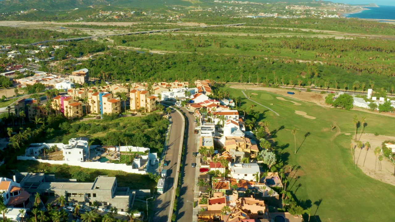 Aerial road and neighborhood view with golf fairway, palms, and distant hills.