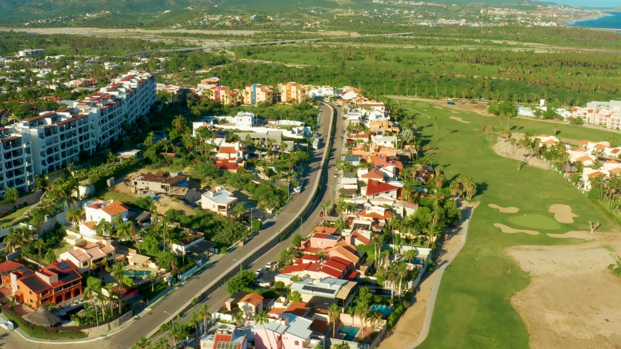 High aerial view along a road beside homes and golf greens.