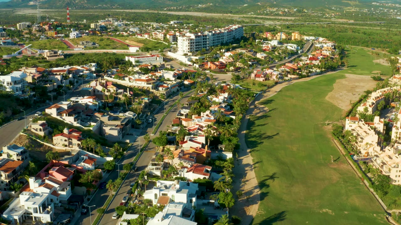 San Jose Del Cabo aerial frame with a green fairway at right, a sandy golf course section, homes along curving streets, and no visible people.
