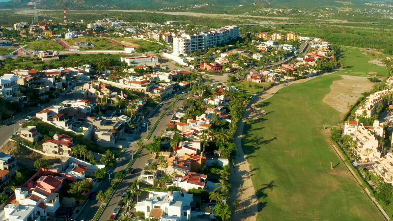 Wide drone view of homes, roads, and golf course.