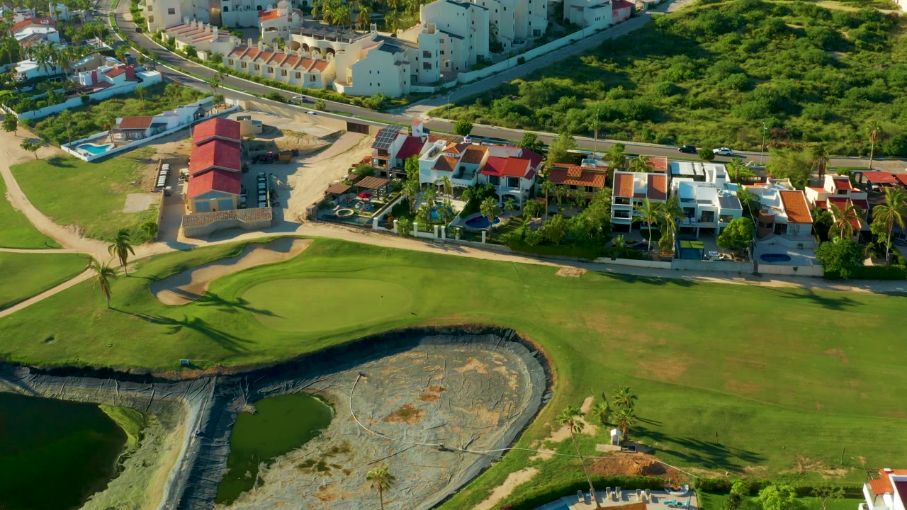 Drone view of fairway grass, sand trap, water hazard, road, and homes.