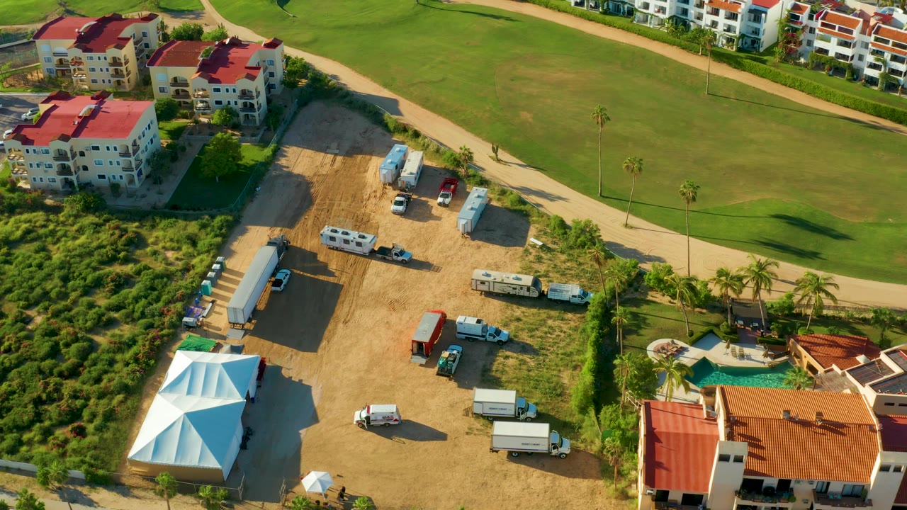 Overhead oblique view of a green field, road, buildings, and construction vehicles.