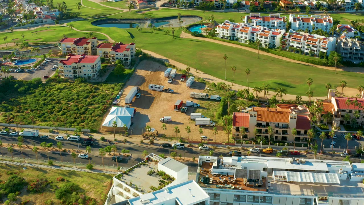 Aerial view of golf grass, residential buildings, sandy lots, trucks, and traffic.