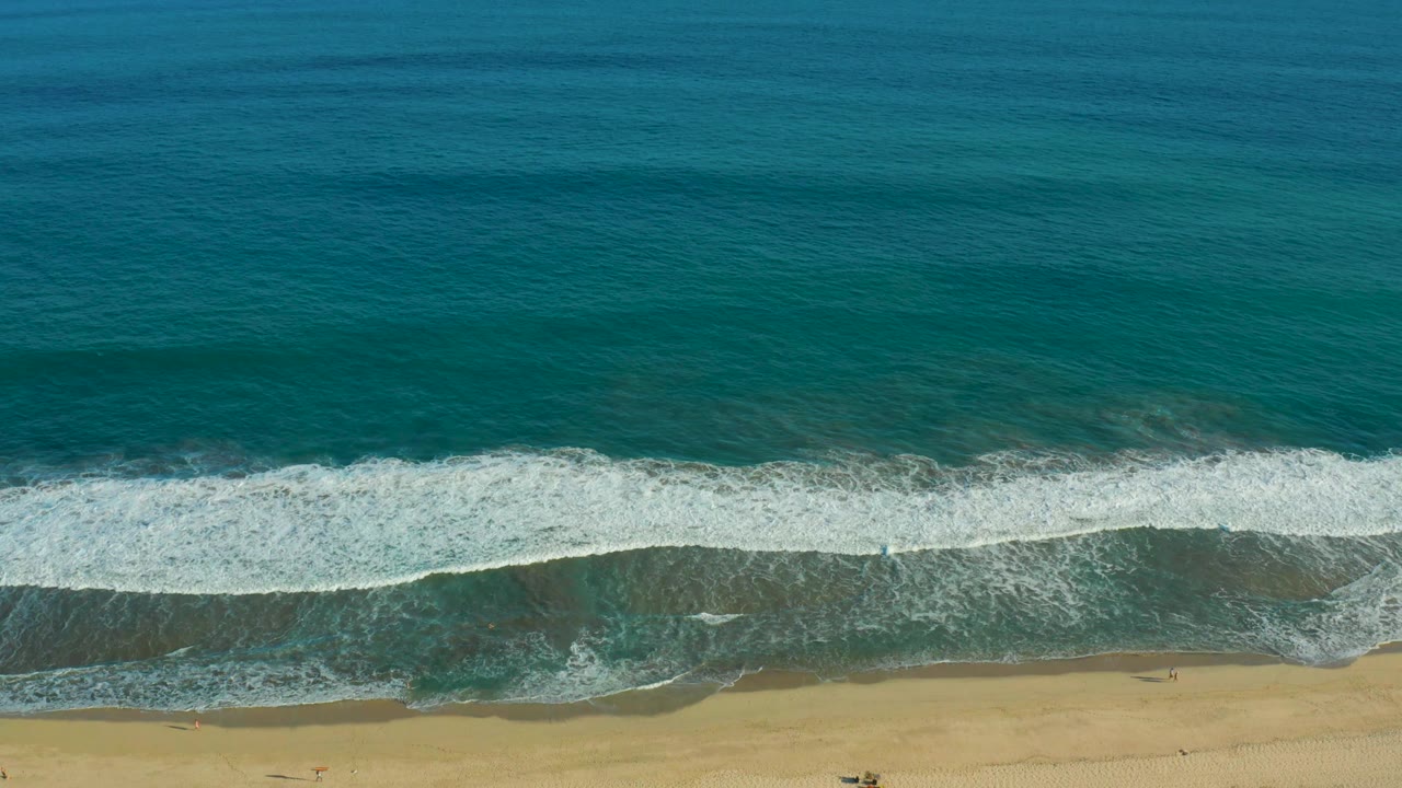 Overhead San Jose del Cabo beach frame where the white foam line sits lower on the shore and darker wet sand appears beneath the wave, with no visible people.