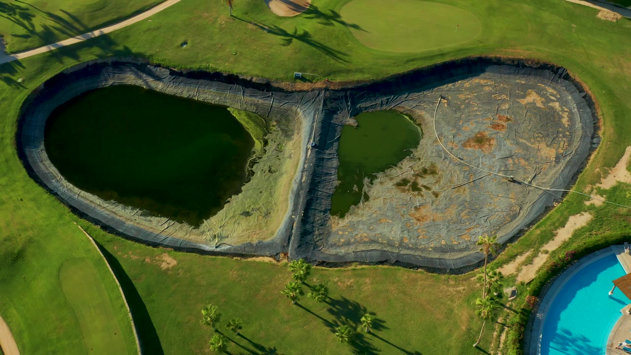 Aerial view of dark lined ponds beside grass and a blue pool edge.