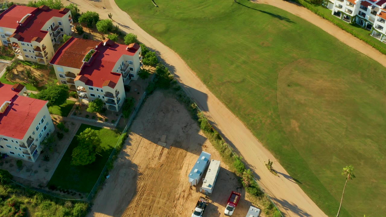 Drone view of villas with red roofs beside a tan path and grass.