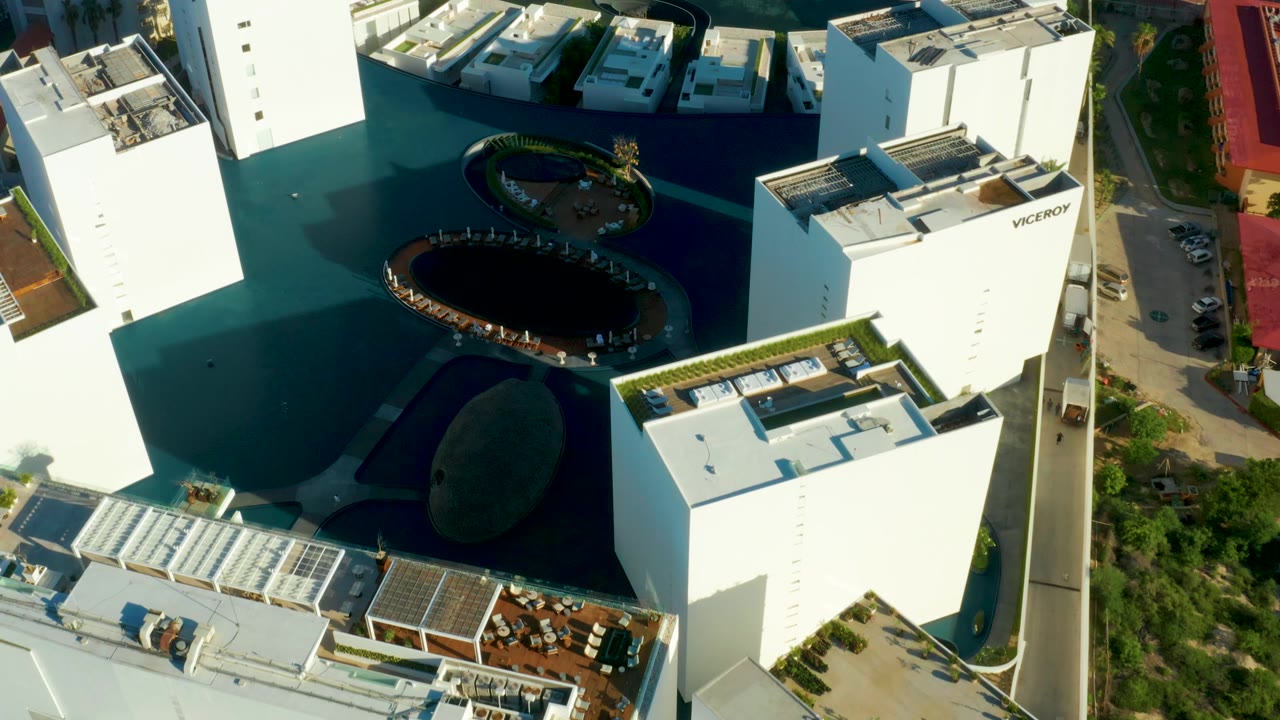 Aerial view with white buildings, dark pool feature, landscaped island, and road.