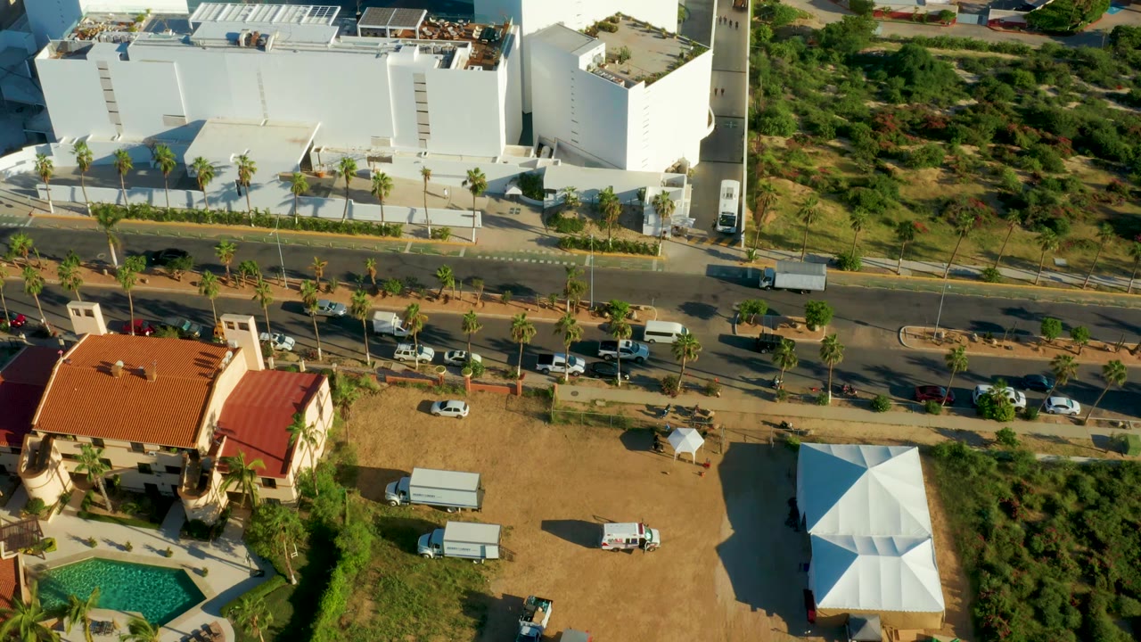 Aerial view centered on white building, road traffic, red-roof house, and dry residential lots.