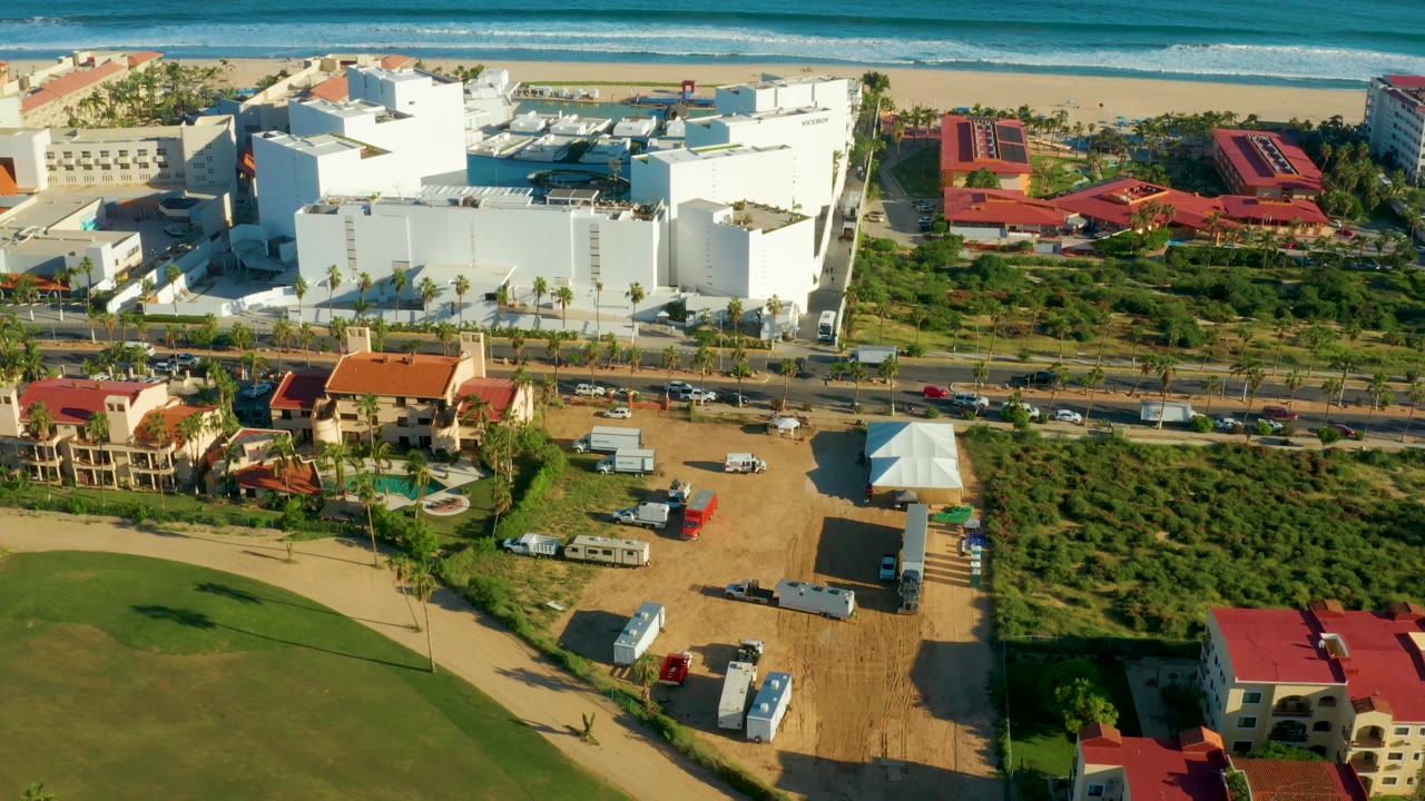 Drone view of coastal buildings, road traffic, trailers, and ocean.