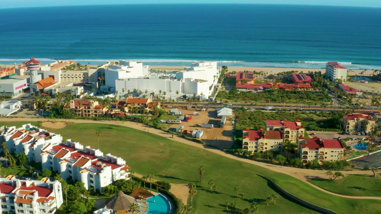 Aerial view of ocean, beach, resort buildings, lawns, and red roofs.