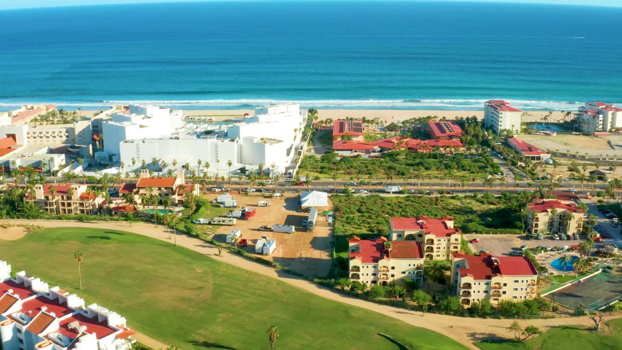 Wide drone view of resort buildings, lawns, beach, and ocean shoreline.