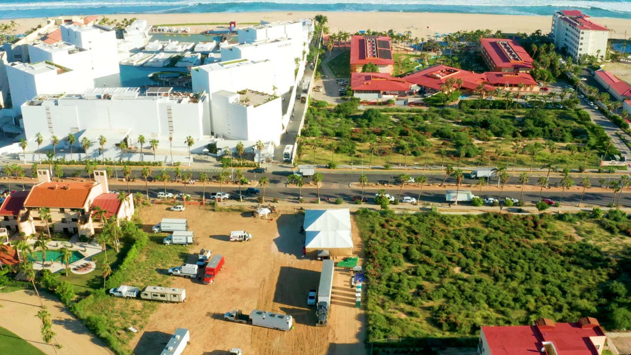 Drone view of beachfront blocks, red roofs, road traffic, and green land by the ocean.