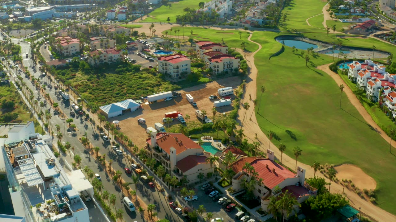 Aerial view of a road beside a golf course and red-roof buildings.