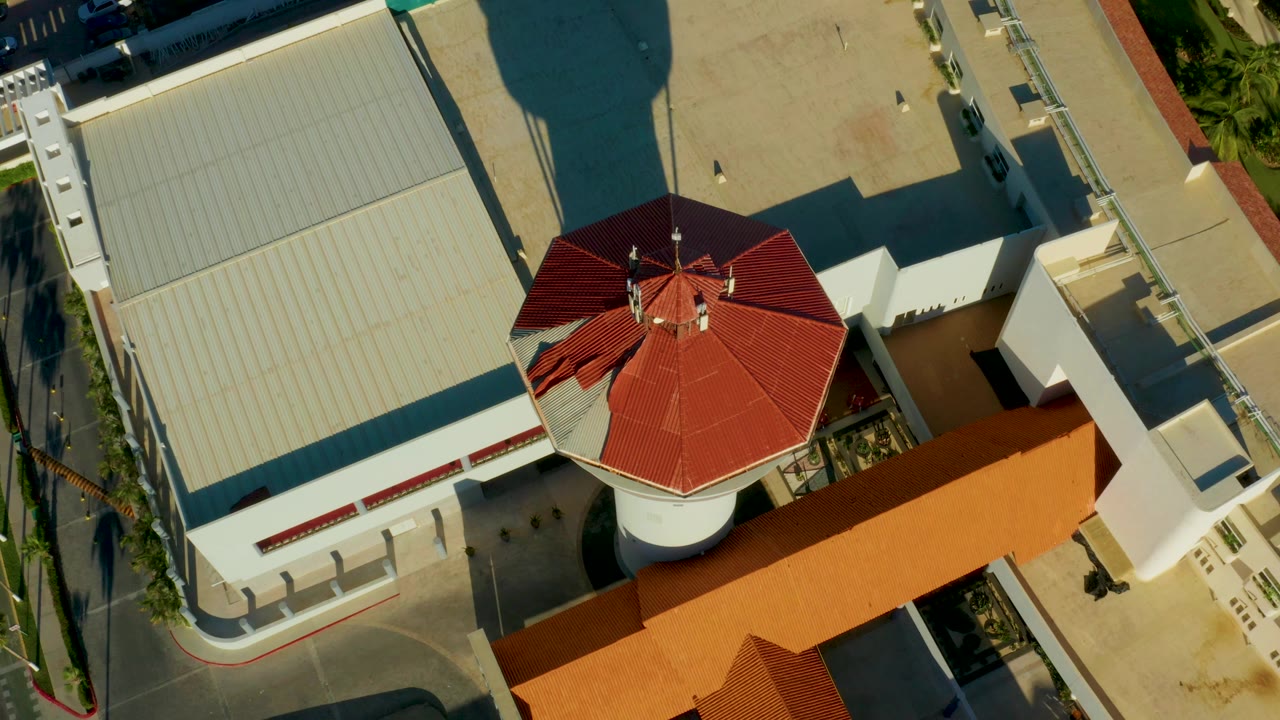 San Jose del Cabo overhead view with the red octagonal roof slightly farther right, bordered by a large pale roof, orange roofline, paved service areas, and no visible people.