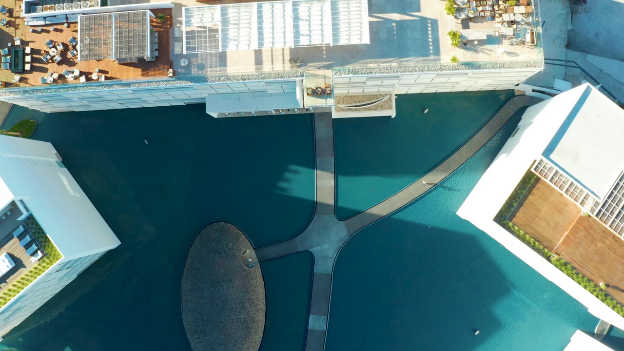 Top-down aerial frame in San Jose del Cabo showing a blue rooftop pool, white rooflines, a curved walkway, terrace decking, and no visible people.