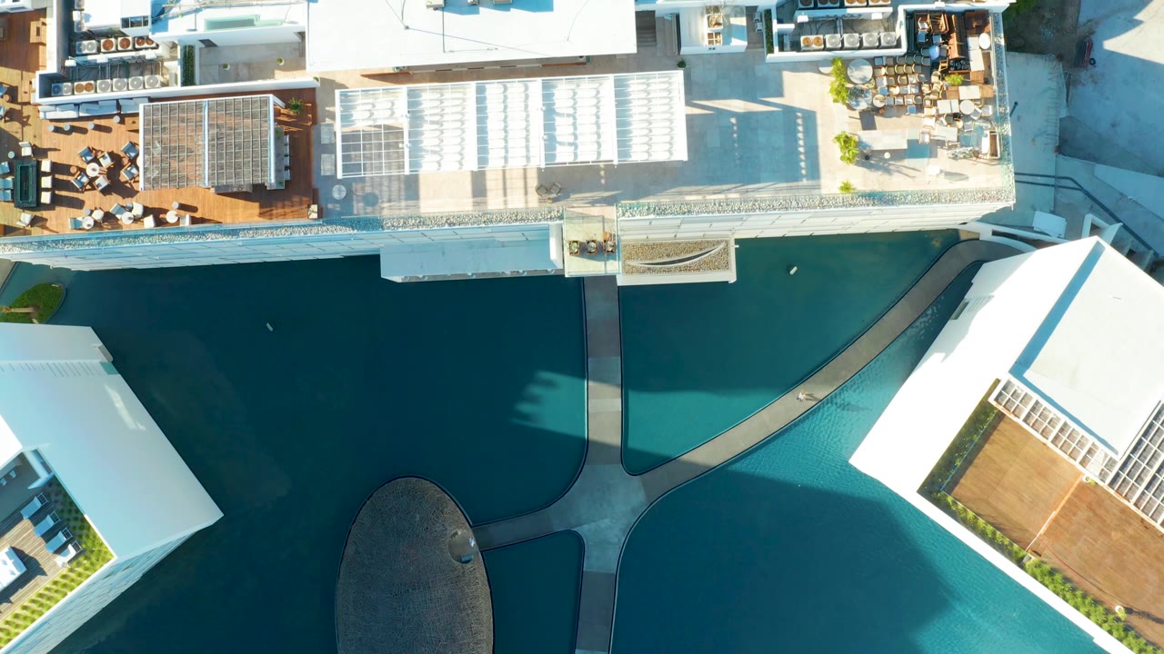 Aerial overhead frame in San Jose del Cabo showing the pool beside a white building corner, rooftop seating areas, gridded shade structures, and no visible people.