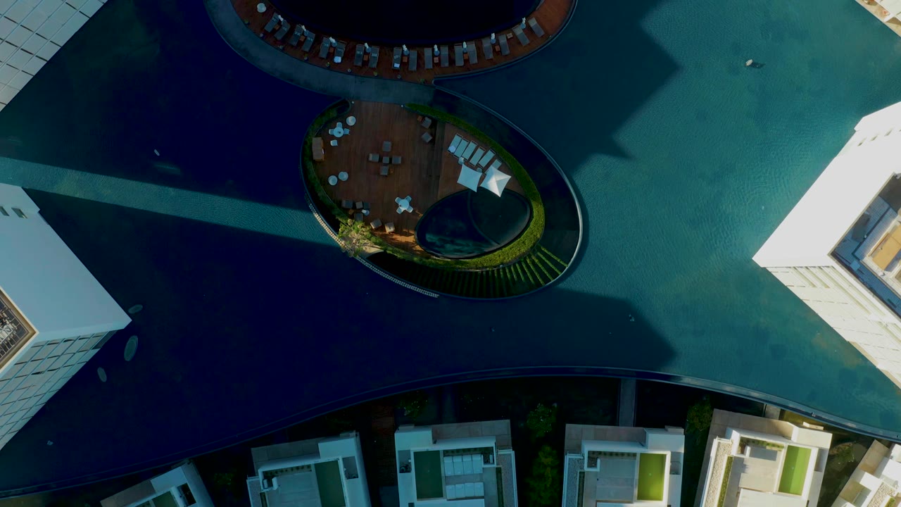 Overhead view of circular pools, lounge chairs, white buildings, and blue-green water.