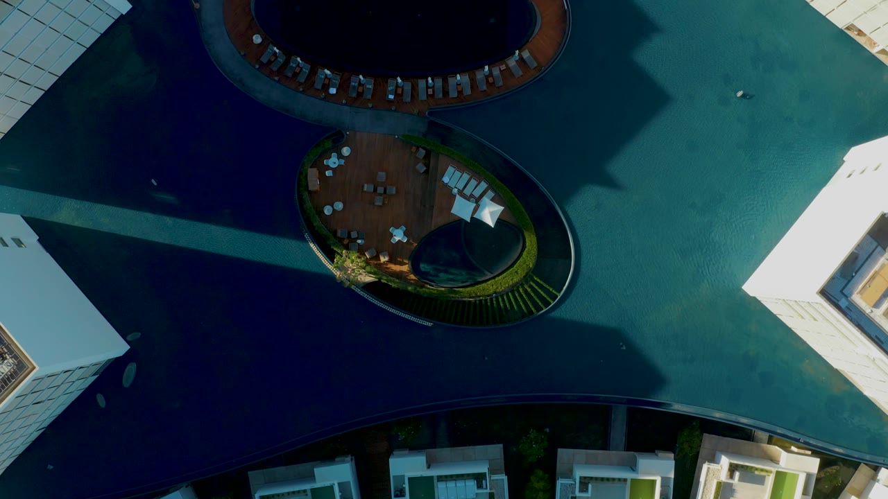 Top-down San Jose Del Cabo frame with more of the upper circular pool visible, lounge chairs along its rim, the lower deck below, sharp sunlight on white walls, and no visible people.