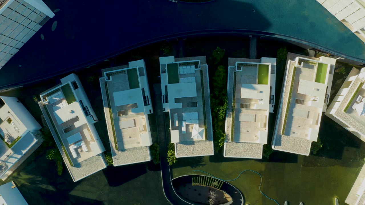 Overhead view of modern white buildings, green courtyard, and curved pool edge.