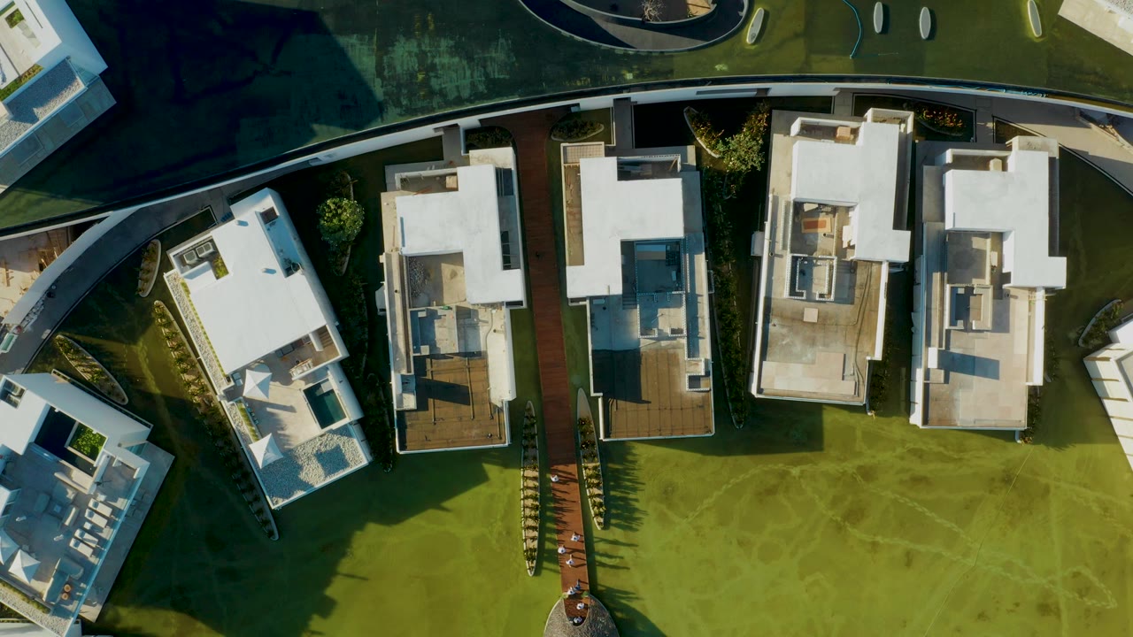 Top-down aerial frame in San Jose Del Cabo showing white flat-roof homes, green lawn areas, curved paths, and no visible people.