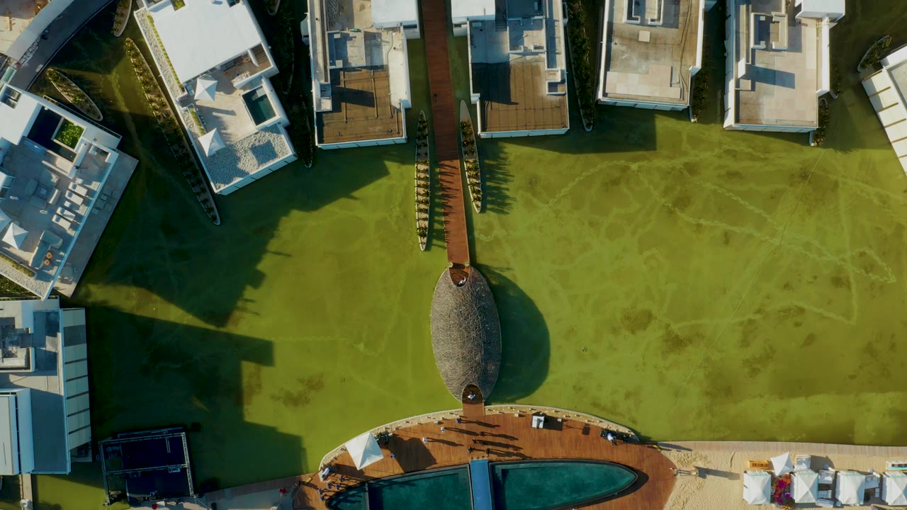 Overhead frame in San Jose del Cabo showing white-roofed modern houses, a green lawn, a central path, part of a curved pool edge, and no visible people.