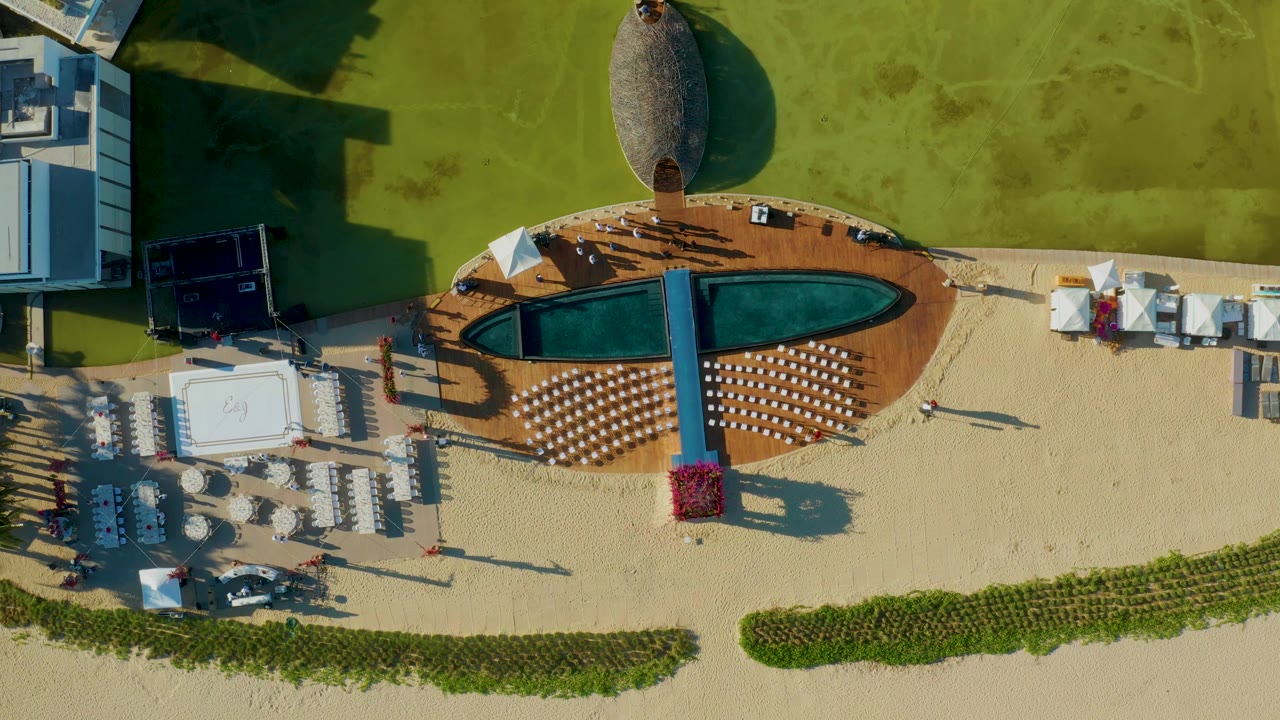 Aerial view of pool deck and beach lounge seating with people and long shadows.