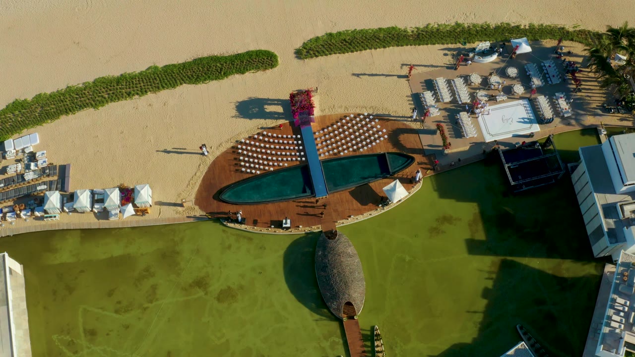 Overhead resort deck with pool, loungers, tents, beach, and lawn.