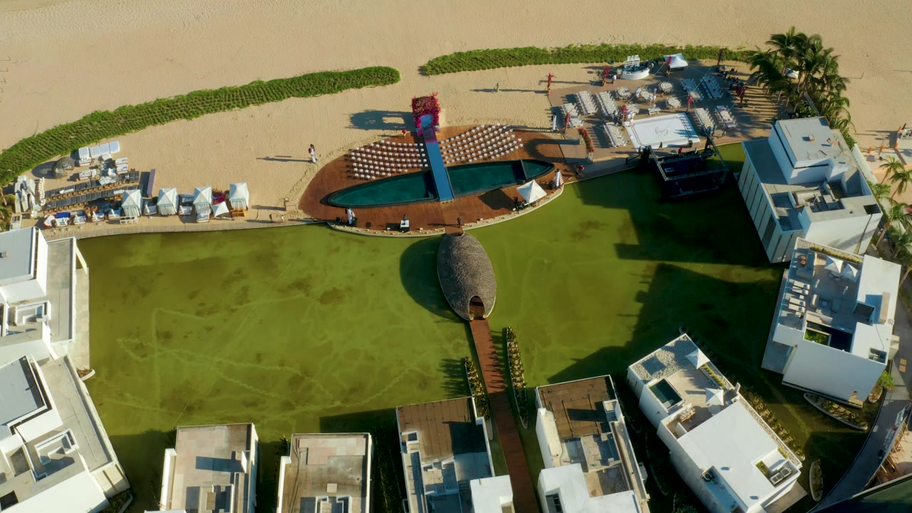 Top-down resort lawn with pool deck, thatched hut, and beach chairs