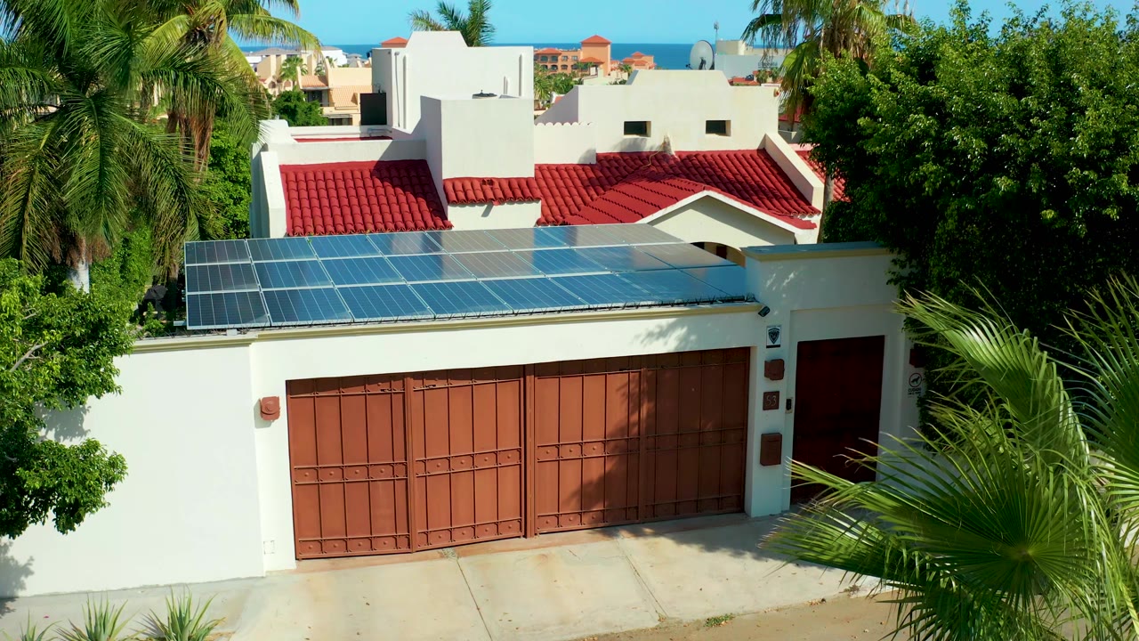 Residential garage and solar roof panels partly framed by palm fronds.