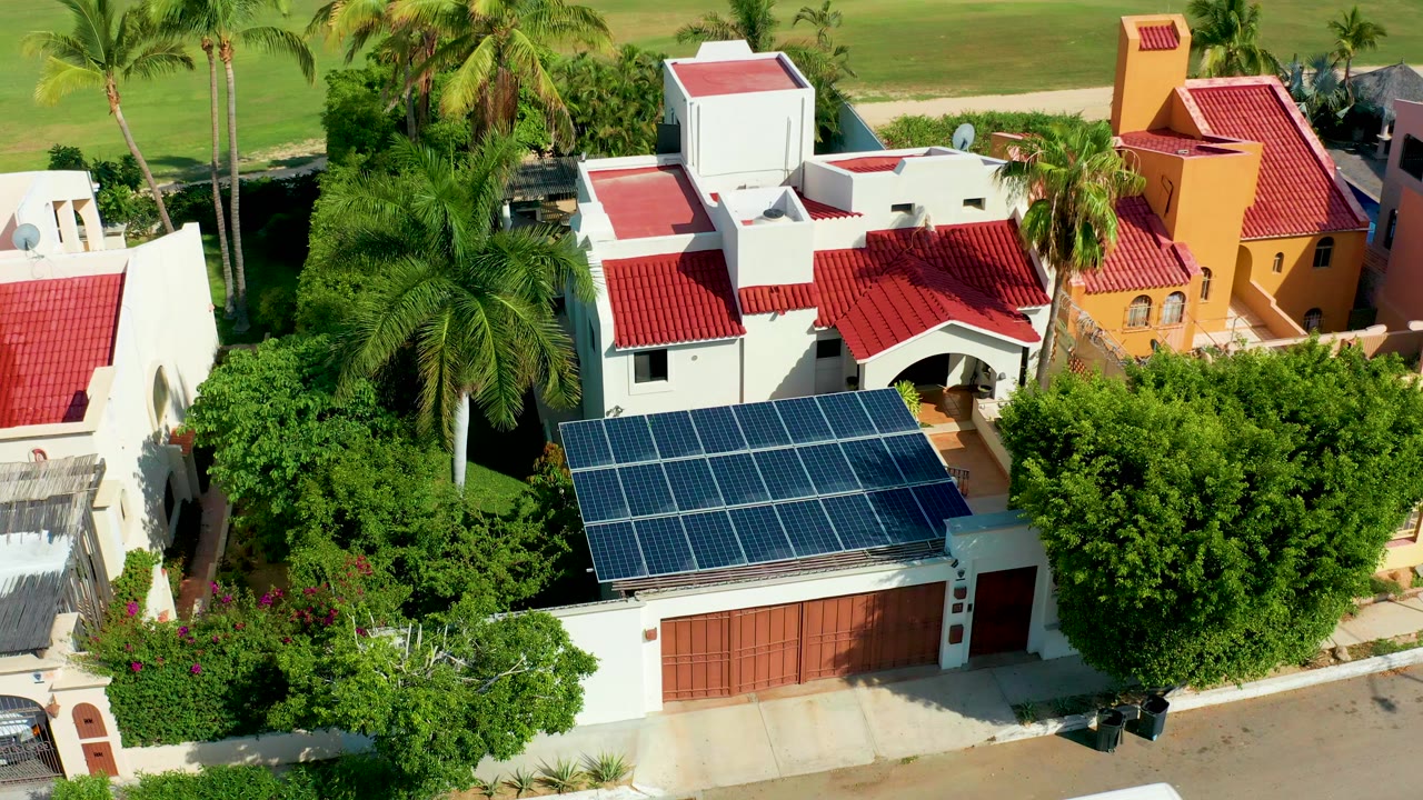 Overhead view of the solar-panel roof with palms and adjacent red-roof buildings.