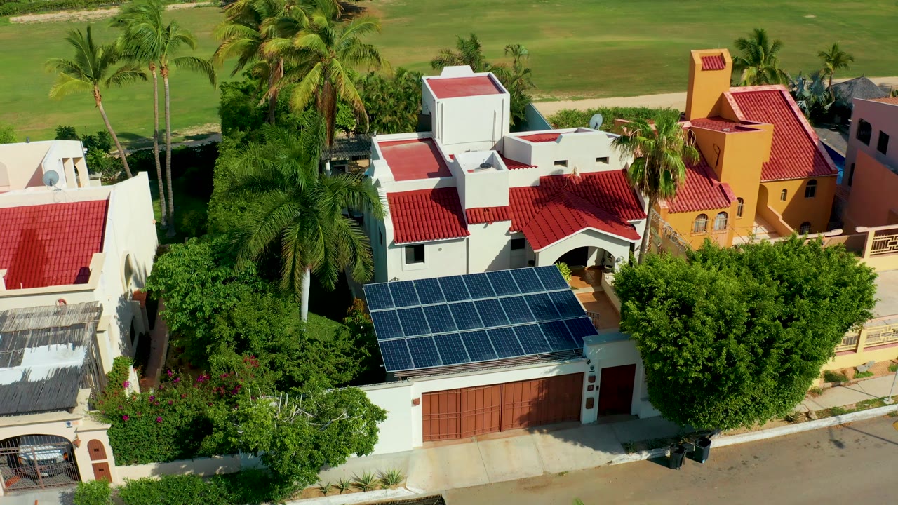 Aerial frame of villas with palms, solar panels, and shifting sunlight.