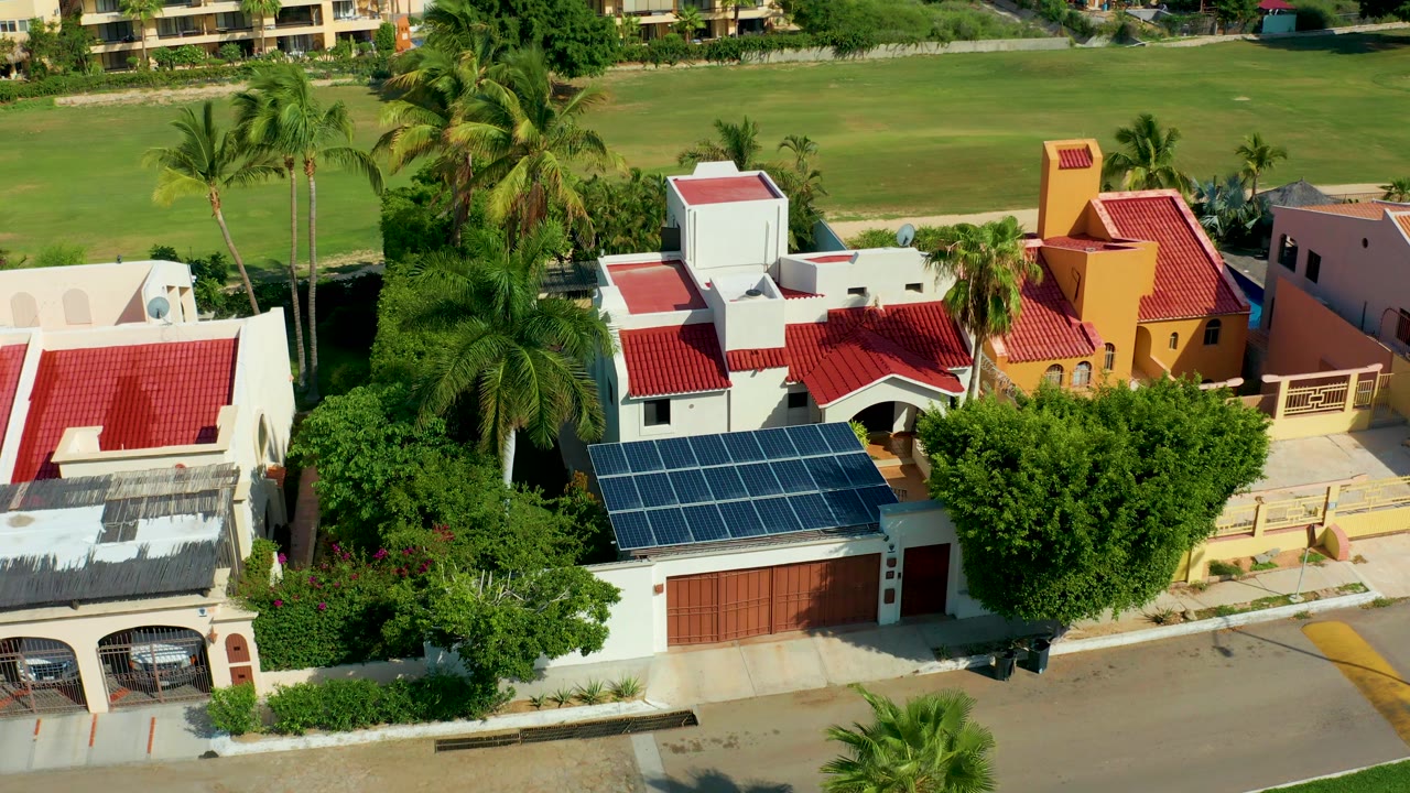 Aerial view of houses with solar panels, red roofs, palms, and a road.