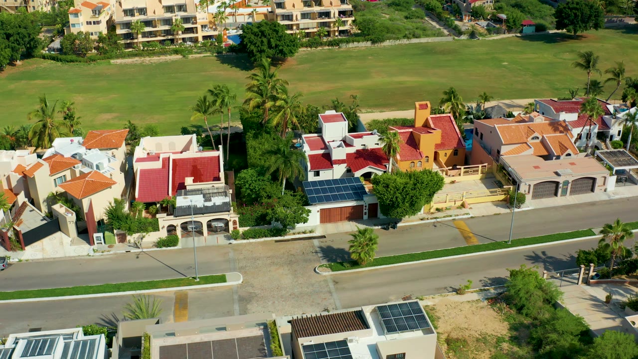 Residential homes with red roofs, palm trees, road, and green field from above.