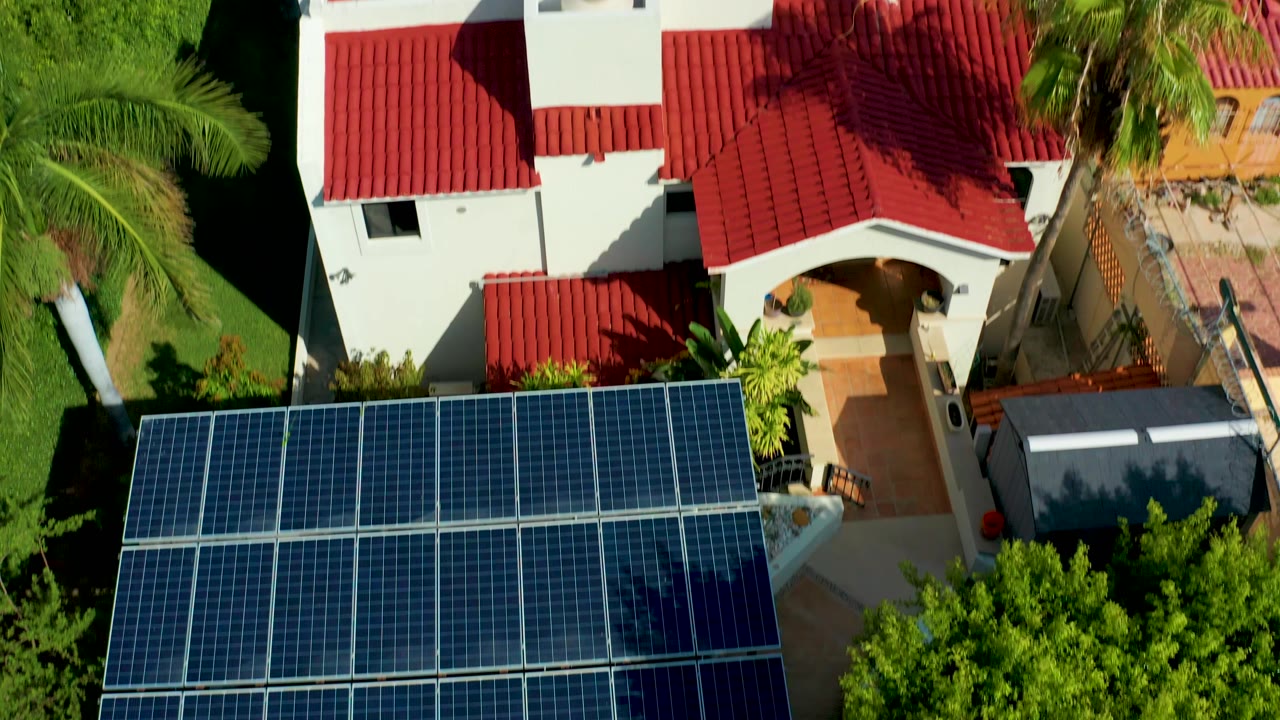 Solar-panel structure below a white house with red roof tiles.