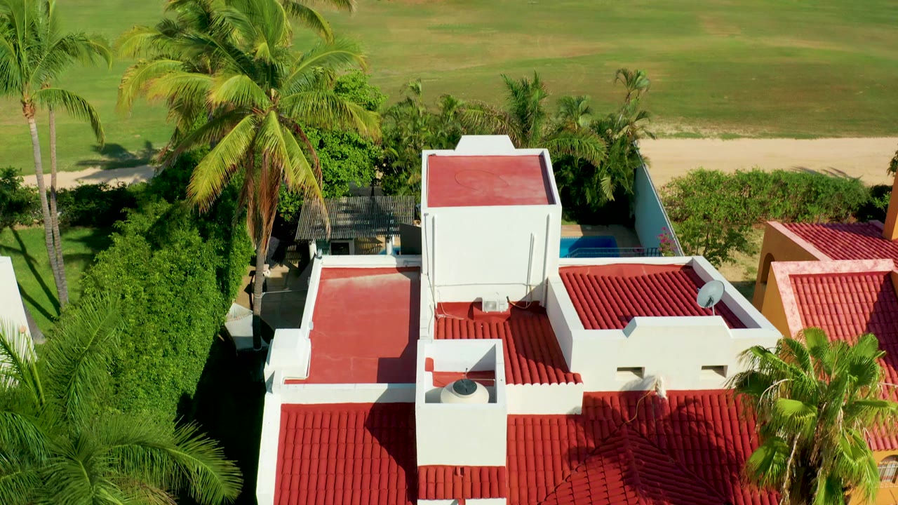 Aerial view of red roofs, palms, hedges, and a grassy area.