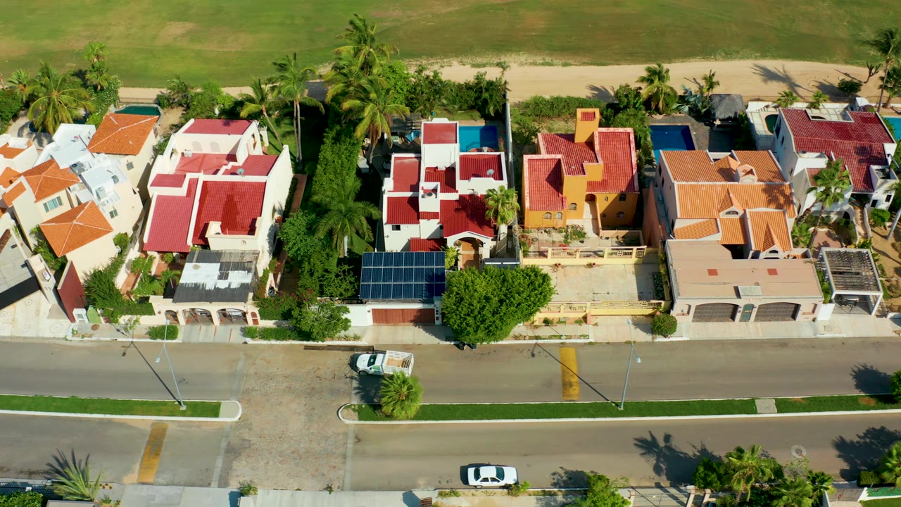 Drone view of houses, palms, and a white car near the curb.