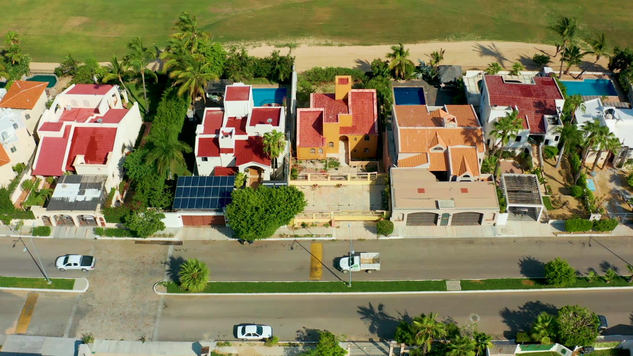 Aerial view of colorful rooftops, palm trees, pools, and cars on a road.