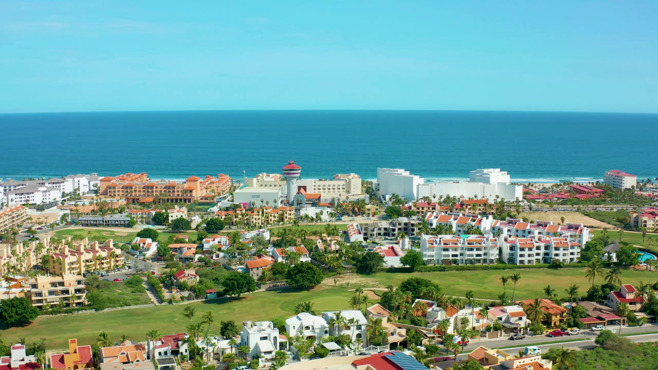 Residential coastline aerial with lawns, homes, and ocean backdrop.