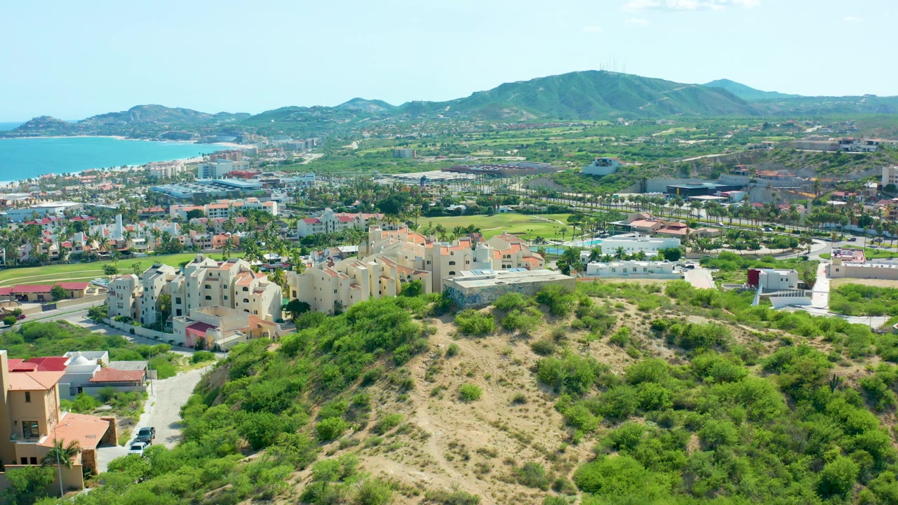 Wide aerial of residential hillside beside ocean and mountain range