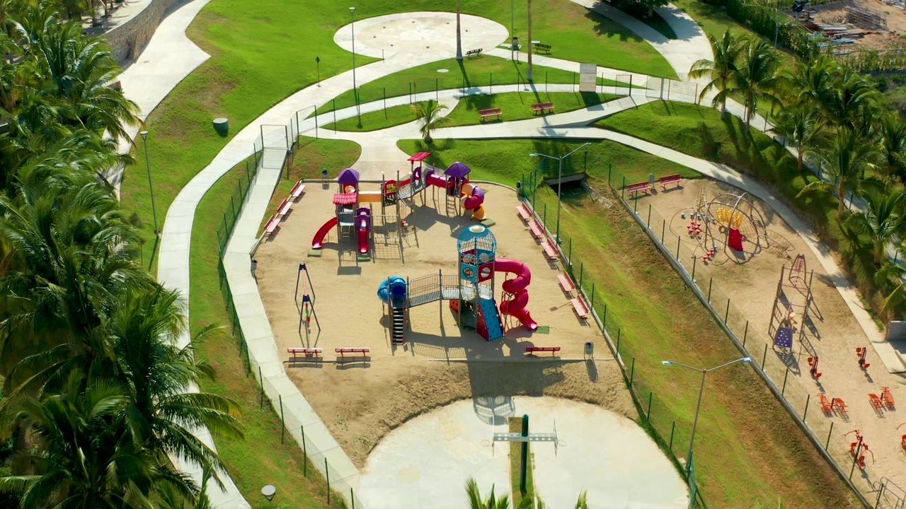 Overhead park playground framed by palms, grass, paths, and fencing.