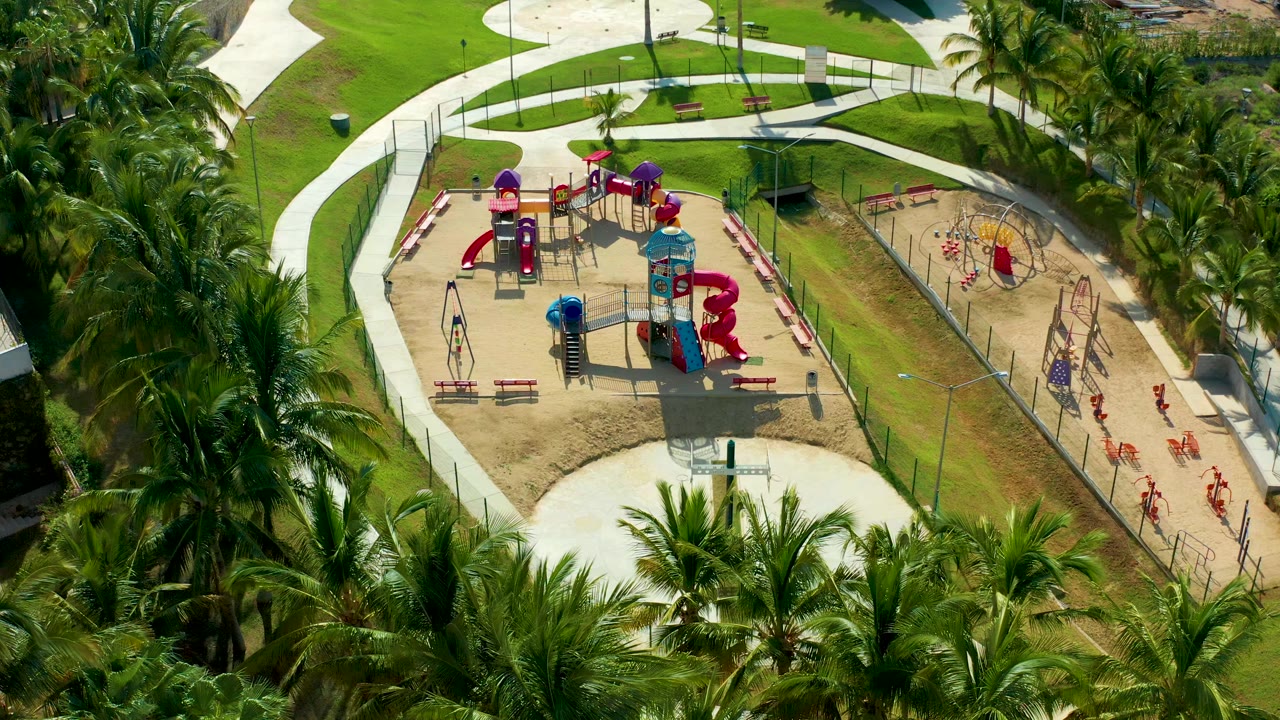 Aerial playground view with palms, paths, grass, and fenced play areas.