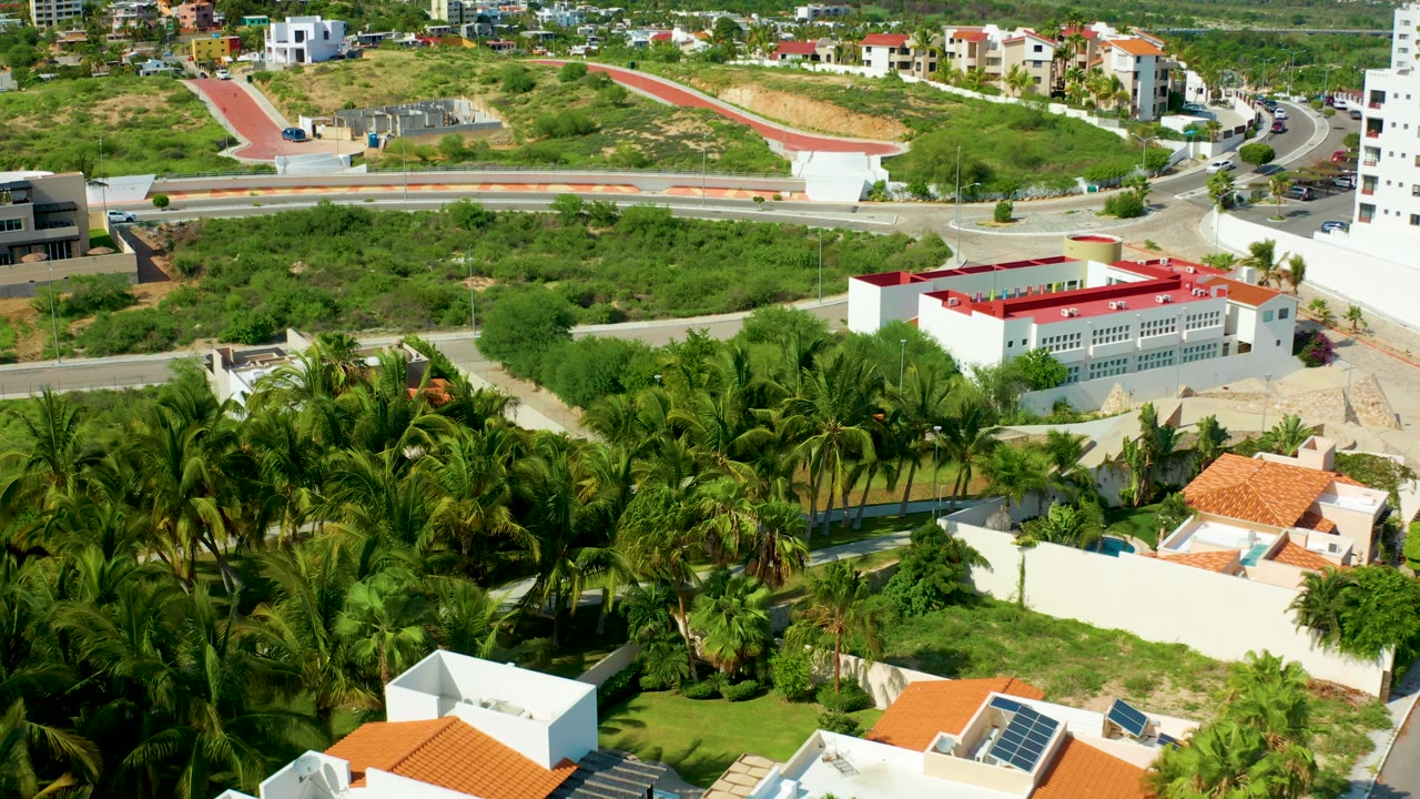 Aerial view of white buildings, palms, roads, and hillside housing.