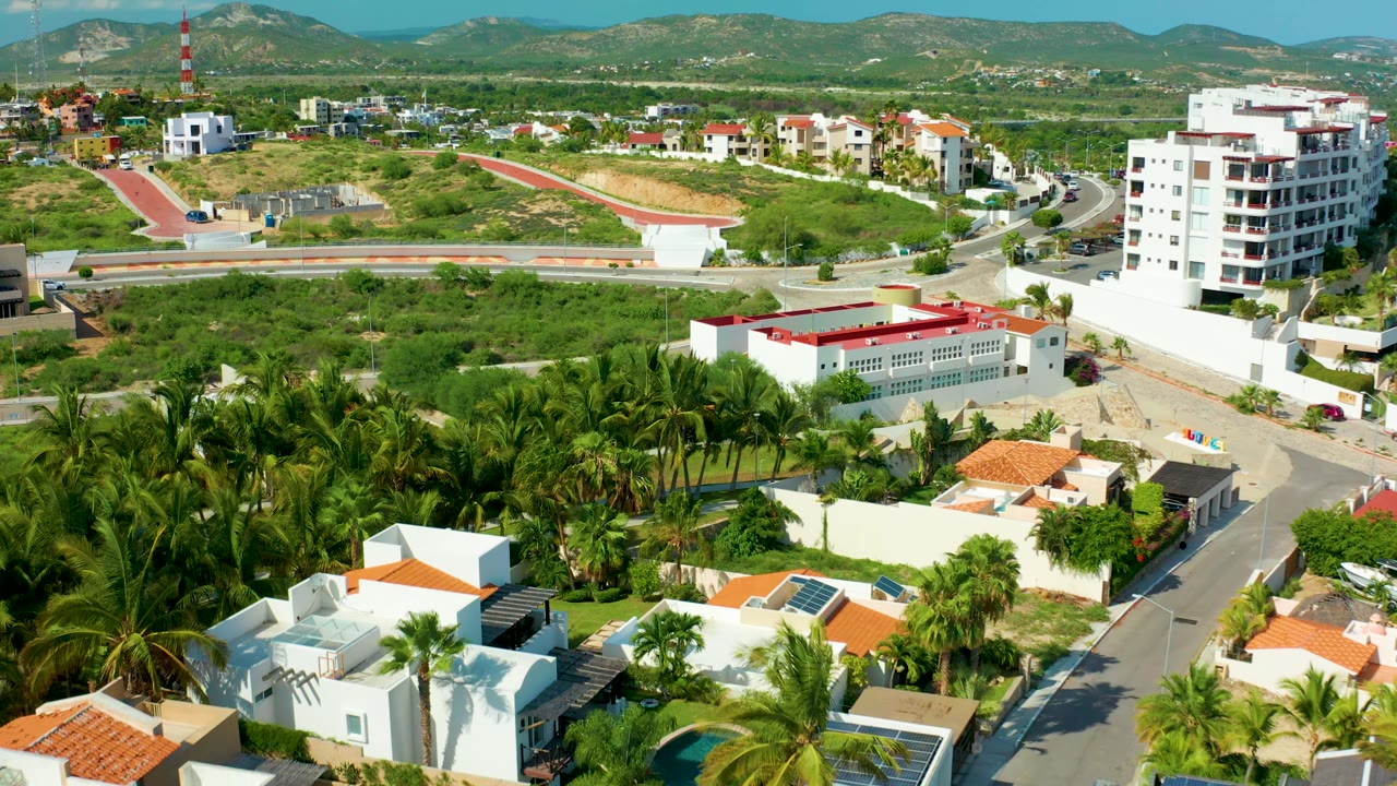 Residential aerial with palms in front, red-roofed buildings midframe, and hills on the horizon.