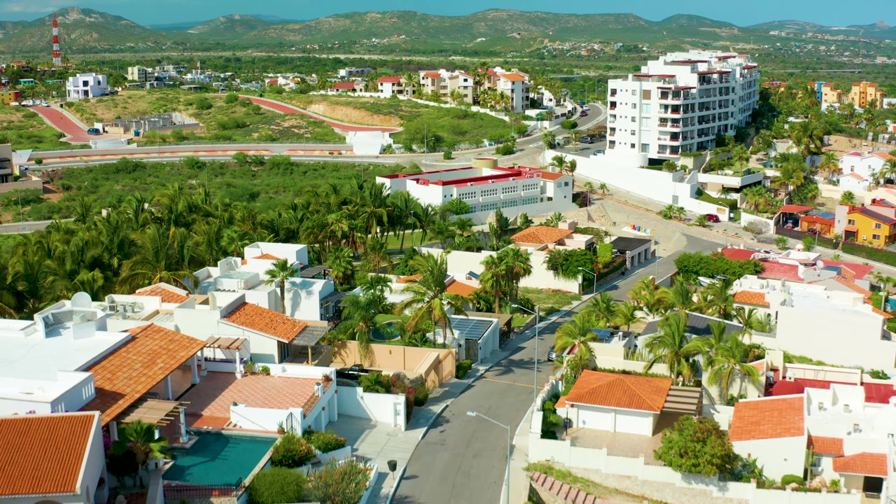 Aerial neighborhood view with white homes, palm trees, roads, and a taller building.