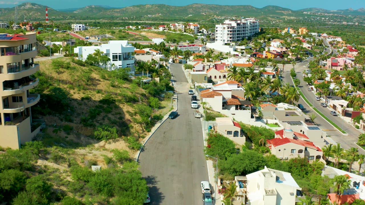 Aerial view of hillside homes, road traffic, and mountains beyond the neighborhood.