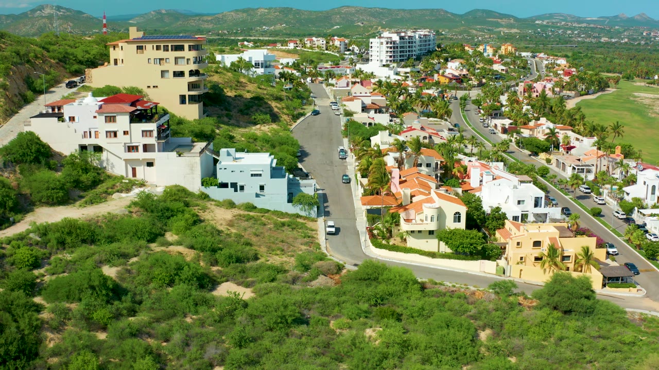 Aerial hillside scene with beige and white buildings beside a winding road.