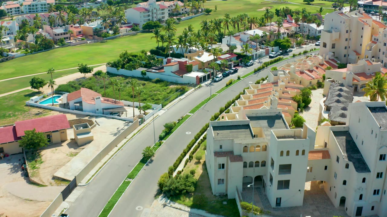Drone view over a residential street with fields and low houses.