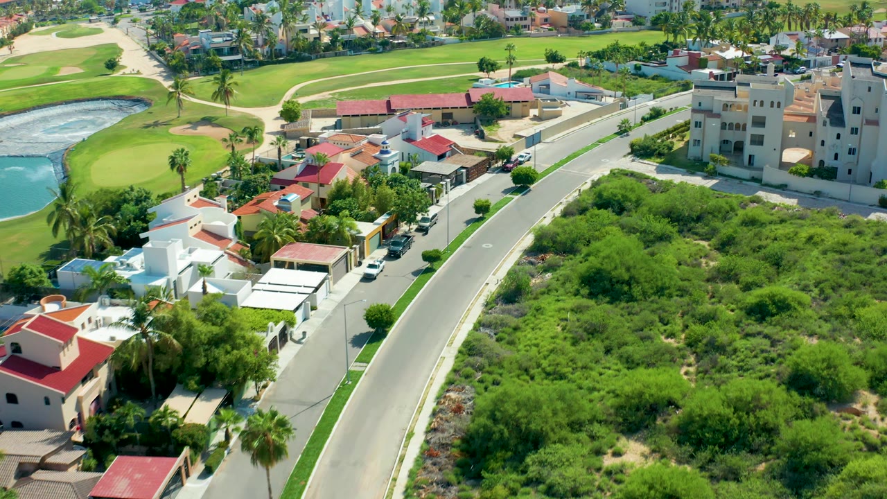 Aerial view of houses, a road, green vegetation, and golf course features.