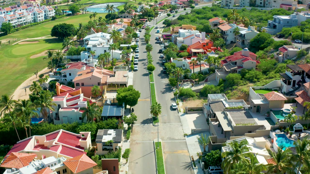 Drone view over homes and a golf course with cars along the street.
