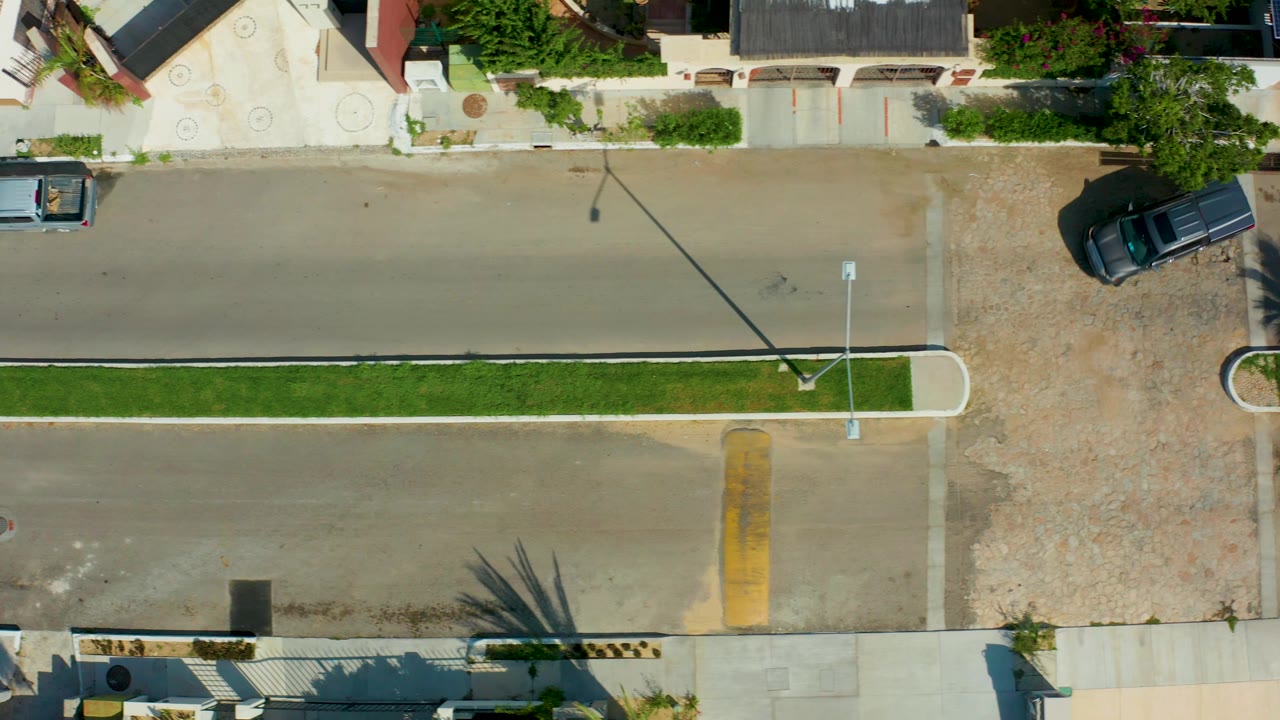 Straight-down street view with pickup on the upper road and dark vehicle by a driveway.